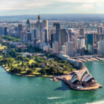Sydney Opera House with Sydney Tower and city skyline in the background, Sydney Harbour and a boat cruising in the foreground.