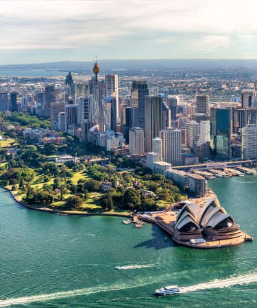 Sydney Opera House with Sydney Tower and city skyline in the background, Sydney Harbour and a boat cruising in the foreground.